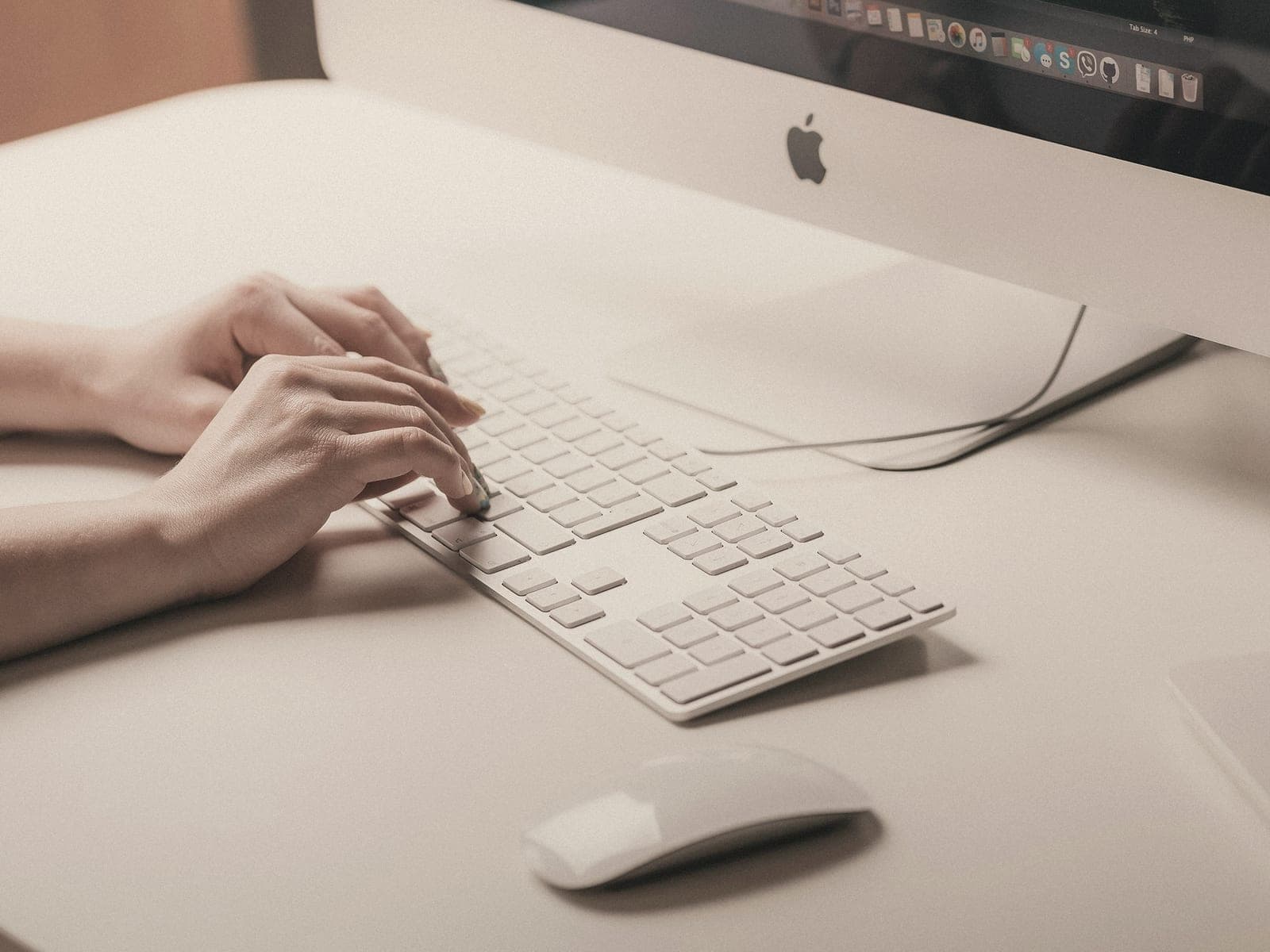 Hands typing on a white keyboard in front of a desktop computer