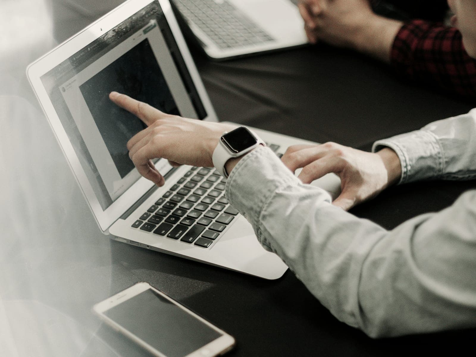 A hand pointing at something on a laptop screen while a colleague types