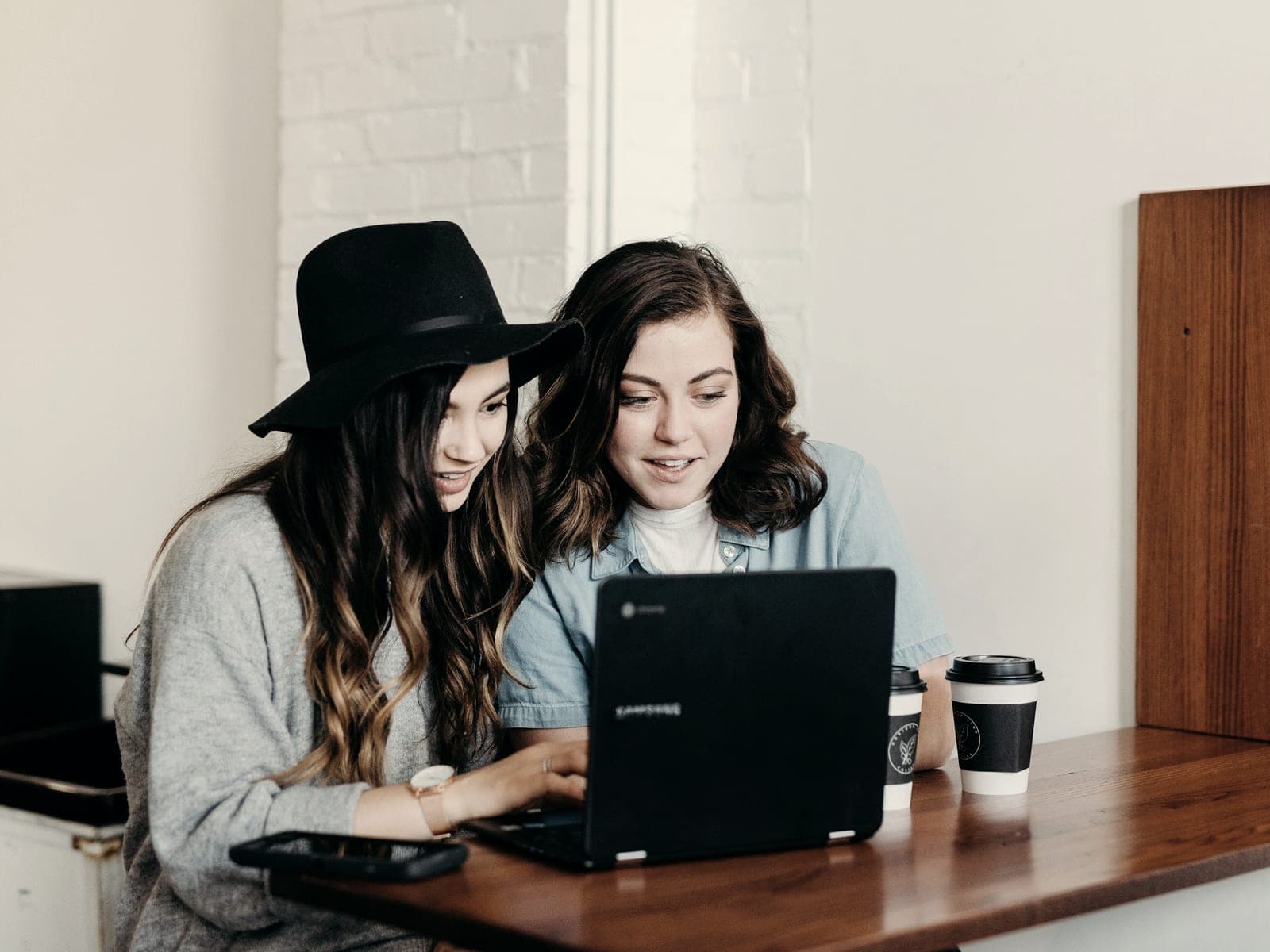 Two people working through something together on one laptop at a wooden table